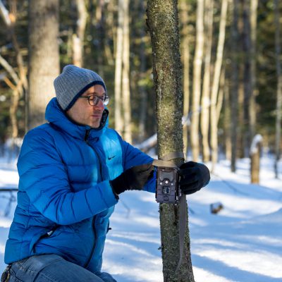 alessio mortelliti setting up trail cam on a tree outside in the snow