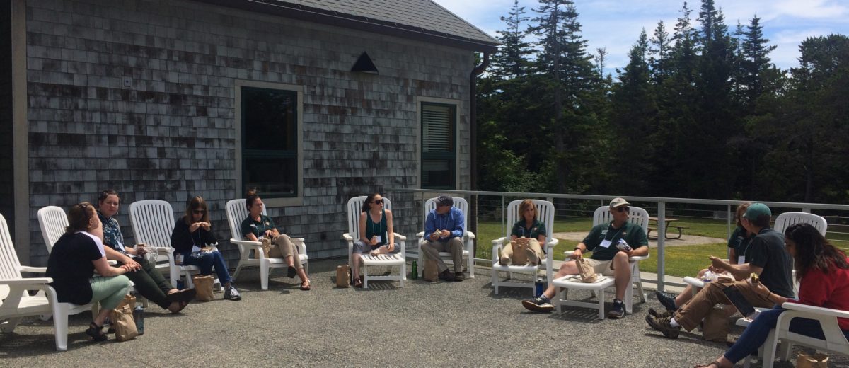 people sit in a semicircle in chairs outside