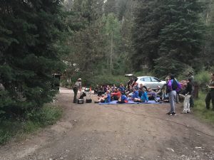 A park ranger delivers a bat program to a group of visitors sitting in a dirt road.