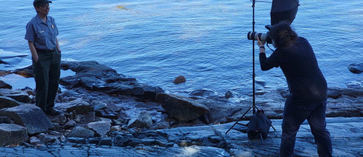 Elliot Higger photographs a person in National Park Service uniform on rocks at the edge of the sea