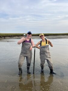 two people standing in shallow water, wearing waders, and smiling